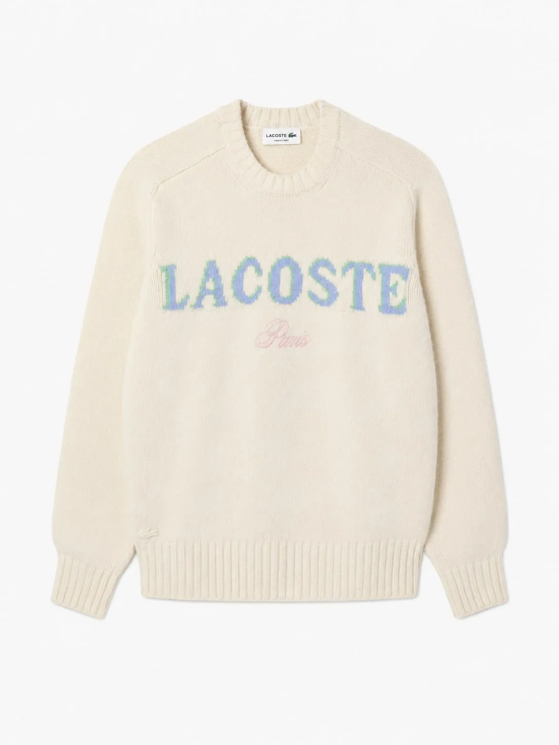 Buzo Lacoste de lana color crudo, vista frontal con el nombre Lacoste tejido en azul y verde y la palabra Paris en rosa debajo
